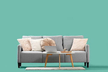 Coffee table with laptop and decor near stylish grey sofa on green background