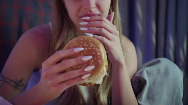 Woman eating burger and watching TV in evening setting