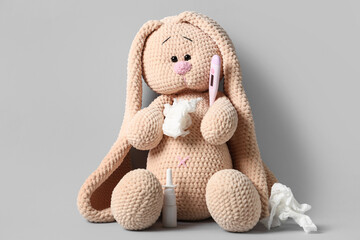 Toy bunny with thermometer, nasal drops and tissues on grey background