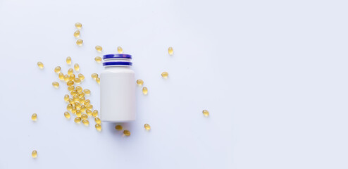 white plastic bottle of dietary supplements with scattered golden fish oil capsules on clean light background with copy space concept of healthcare pharmacy wellness nutrition
