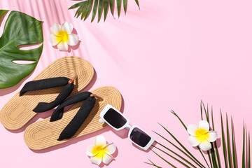 Summer composition with beach accessories, plumeria flowers and tropical leaves on pink background
