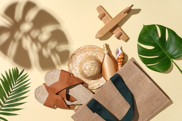 Composition with bag, beach accessories, wooden airplane and tropical leaves on beige background