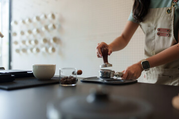 Barista pressing coffee grounds with tamper in cafe