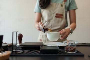 Barista pouring filter coffee into cup at cafe counter