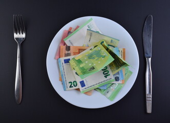 Crumpled euro banknotes on white plate with fork and knife on black