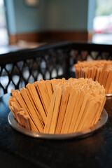 A close-up of wooden coffee stirrers placed in a round container on a table in a cozy cafe...