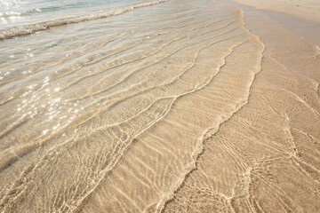 Gentle Ocean Waves Washing Over Sandy Beach. Close-up of soft waves lapping against a smooth sandy shore under warm sunlight, capturing a peaceful coastal moment
