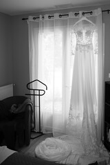 white wedding dress hanging front windows in beding room