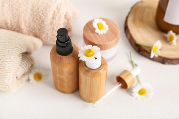 Chamomile flowers, towels, bottles and jar of cosmetic products on white background, closeup