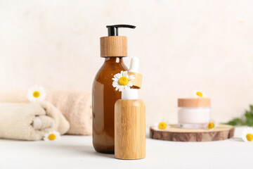 Chamomile flower and bottles of cosmetic products on table near beige wall, closeup