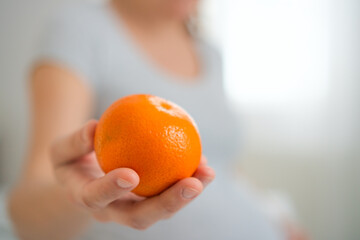 Expecting mother holding fresh orange while gently caressing her baby bump. Peaceful moment of...