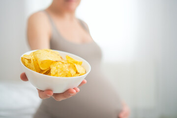 Close-up of future mother snacking on potato chips while stroking her baby bump. Honest portrayal...