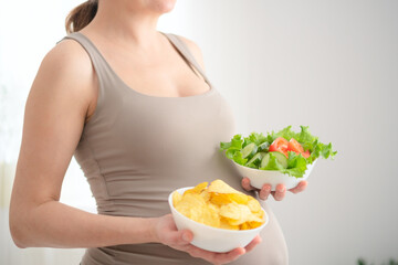 Future mother contemplating between nutritious salad and tempting chips. Honest portrayal of...