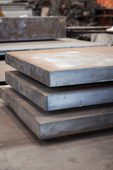 Stack of thick, rectangular metal plates with a dark, gray-blue hue, showcasing a metallic texture and industrial look for fabrication.