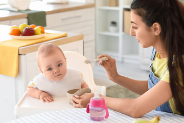 Mother feeding her baby in high chair at home