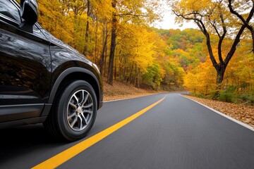 Black car driving on asphalt road lined with autumn trees displaying vibrant yellow foliage