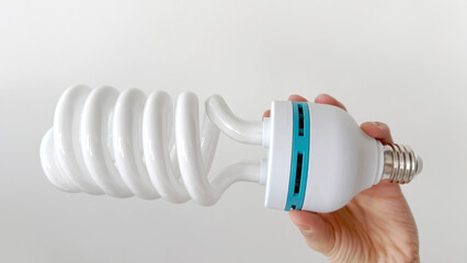 Hand holding a large spiral compact fluorescent light bulb (CFL) with E27 base on white background....