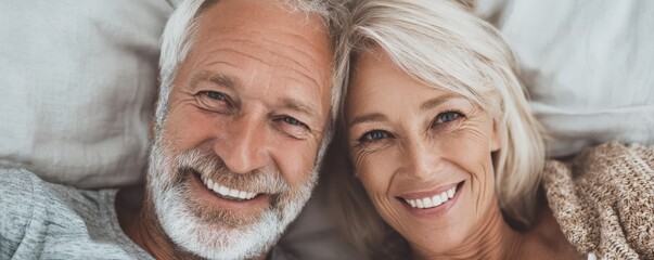 Smiling elderly couple lying close together on a bed, showing warmth and happiness.