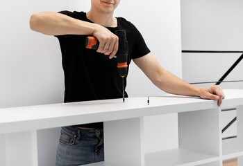 A young craftsman assembles furniture fittings. Screwing the confirmat close-up. Professional furniture assembling. Installation of new furniture. Furniture assembly