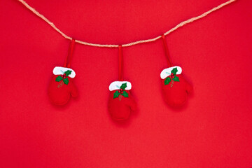 Red gloves hanging on a rope isolated on the red background with copy space. The atmosphere of Christmas and New Year. Christmas banner, mock up