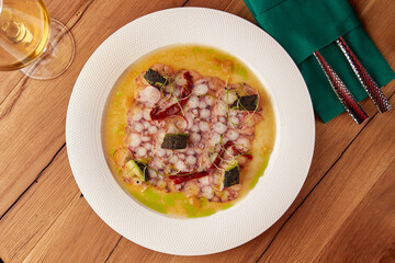 Top view of a plated gourmet octopus carpaccio, garnished with herbs, vegetables, and olive oil, served with white wine.