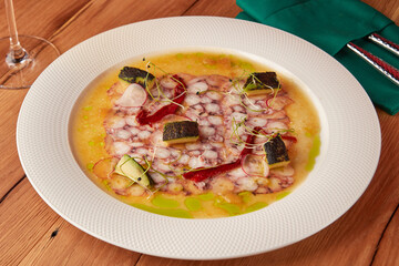 Gourmet octopus carpaccio, garnished with herbs, vegetables, and olive oil, served with white wine.