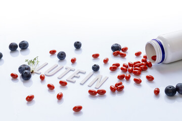 lutein dietary supplement capsules spilled from white bottle with fresh blueberries green leaves and text lutein on clean white background concept of eye health antioxidant natural vitamin nutrition