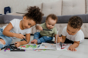 three African-American children are lying on the floor and drawing