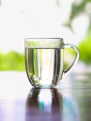Clear glass of drinking water on a table with natural green background.