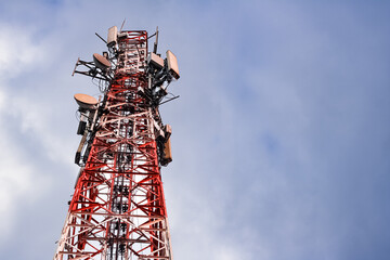 Telecommunication tower with antennas against a partly cloudy blue sky.