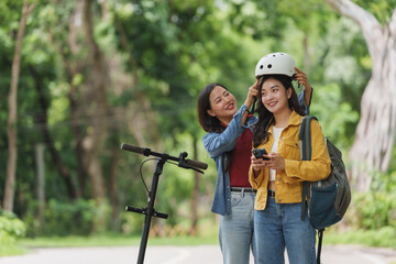 Two young women preparing for an e scooter ride in a park