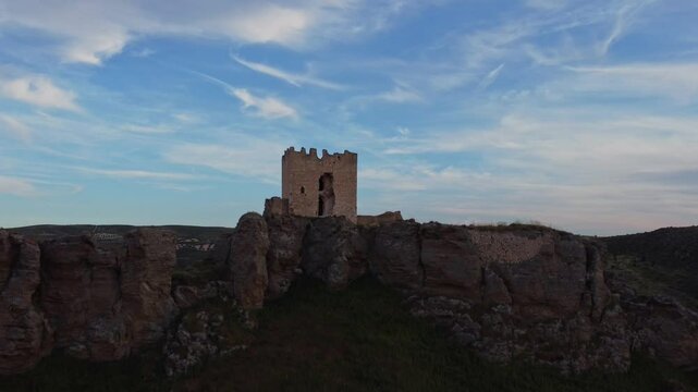 Reveal Drone shot of the medieval Oreja Castle perched on a hilltop at golden hour near Aranjuez, Spain. Scenic sunset over rural fields and rocky landscape.