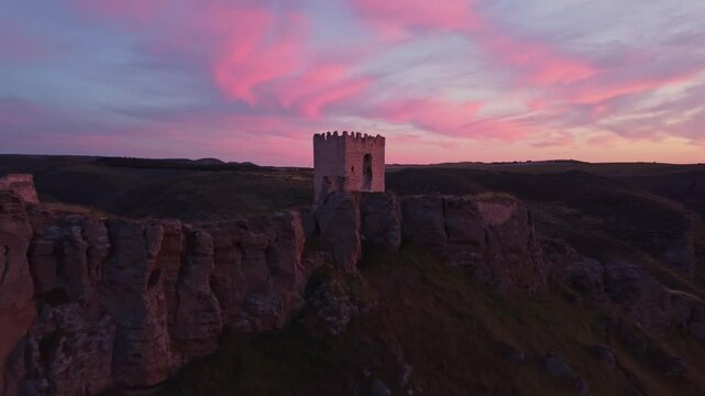 Drone shot of the medieval Oreja Castle perched on a hilltop at golden hour near Aranjuez, Spain. Scenic sunset over rural fields and rocky landscape.