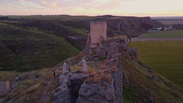 Drone shot of the medieval Oreja Castle perched on a hilltop at golden hour near Aranjuez, Spain. Scenic sunset over rural fields and rocky landscape.