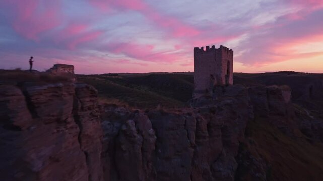 Drone shot of the medieval Oreja Castle perched on a hilltop at golden hour near Aranjuez, Spain. Scenic sunset over rural fields and rocky landscape.