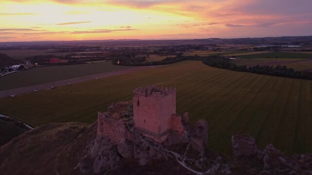Drone shot of the medieval Oreja Castle perched on a hilltop at golden hour near Aranjuez, Spain. Scenic sunset over rural fields and rocky landscape.