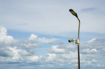 CCTV cameras installed on light poles with clouds as a backdrop. An outdoor CCTV surveillance...