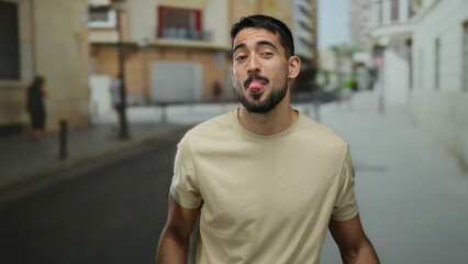 Fototapeta premium Young man smiling playfully in an urban street setting, showcasing a casual style and joyful expression enhancing the vibrant city atmosphere.