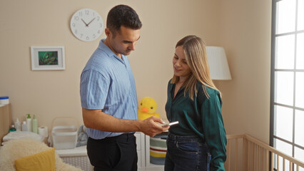 Obraz premium Hispanic couple in bedroom looking at phone near baby crib, showcasing love and family in cozy home setting, surrounded by warm interior decor.