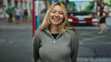 Woman smiling in city street with blurred pedestrians and bus in the background suggests a lively...