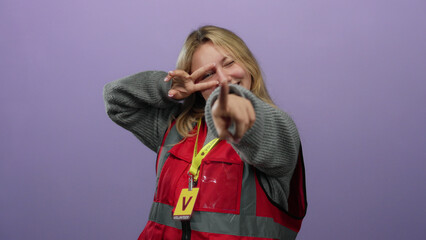 Blonde woman volunteer smiling and pointing in front of isolated purple background wearing a red...