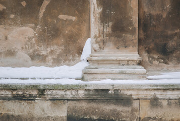 Lower part of an old column (pilaster). Snow-covered architectural element against a beige stone...