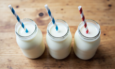 Top-Down View of Three Milk Bottles with Blue, White, and Red Straws on a Wood Plank