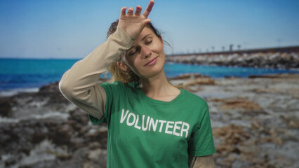 Portrait of woman hand wiping sweat on beach blonde volunteer wearing green shirt beneath sunny...