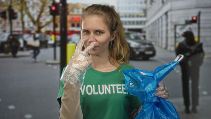 Blonde woman with hand pointing holds a volunteer bag for street cleanup in a city outdoor...