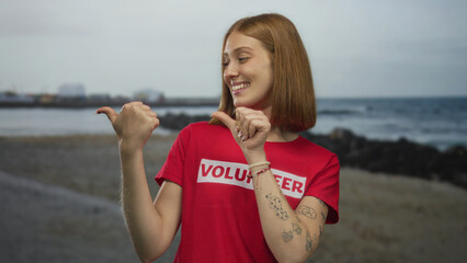 Young blonde woman wearing volunteer shirt points thumbs over shoulder at sandy shoreline;...