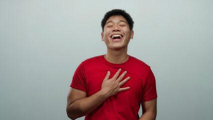 Young chinese man wearing red shirt smiling joyfully against isolated white background in playful expressions exhibiting positive emotions and happiness.