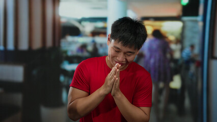 Young man in red shirt enthusiastically gesturing indoors at a bustling hotel setting, adding...