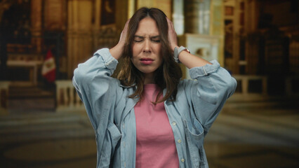 Fototapeta premium Woman feeling stressed in a church setting, surrounded by grand architecture capturing an emotional moment with a peruvian flag, highlighting her hispanic ethnicity and indoor environment.