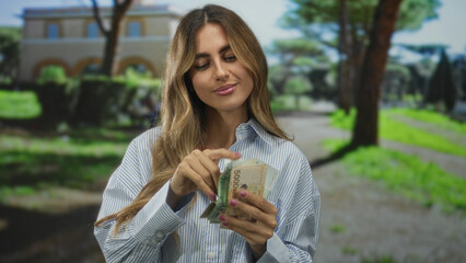 Woman in striped shirt counting banknotes with hands in a sunlit park; wealth planning satisfaction success.
